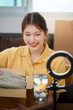© Natee Meepian - Unboxing Experience. Young woman revealing contents of a package during a live stream.