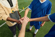 © Mediaphotos - Multiethnic teenage boys and Black male coach standing on soccer field joining hands in team huddle, showing unity and teamwork before match, only upper bodies and hands visible