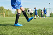 © Mediaphotos - Teenage boys practicing soccer on outdoor field, one teenager kicking ball in foreground while other teenagers and coach standing near cones in background during training session
