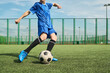 © Mediaphotos - Teenage boy kicking soccer ball on outdoor field, wearing sports uniform, showing dynamic movement during practice or game, lower body and legs visible, action in progress