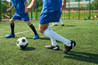 © Mediaphotos - Teenage boys playing soccer on outdoor field, focusing on legs and feet in motion while competing for ball, athletic activity taking place during sunny day, green artificial turf visible