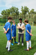 © Mediaphotos - Black man coaching group of teenage boys on outdoor soccer field, holding clipboard and discussing strategy while teenagers listening attentively in sports uniforms