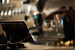 © DragonImages - Digital register terminal placed on wooden counter inside cozy coffee shop with blurred barista and coffee-making equipment visible in background