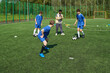 © Mediaphotos - Group of teenage boys practicing soccer drills on outdoor field while Black man coach observing and instructing, soccer balls and training cones scattered on artificial turf