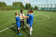 © Mediaphotos - Black man coaching group of boys on soccer field, teenage boys standing in circle stacking hands together, coach leading team building exercise during outdoor practice