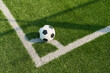 © Mediaphotos - Soccer ball resting on corner of outdoor field, positioned on boundary lines, artificial grass surface visible, no people present, sports equipment in game setting