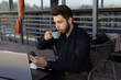© Midea  - The man is drinking from a cup while looking at his phone, with a laptop open