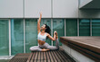 © BullRun - Smiling woman in yoga attire practicing pigeon pose stretch outdoors. Conceptual photo symbolizing balance, flexibility, and the integration of wellness into modern digital lifestyles.