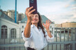 © BullRun - Confident woman in white shirt smiles while waving for selfie. Conceptual photo symbolizing empowerment, individuality, social identity, and modern digital communication.