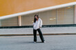 © BullRun - Full-body portrait of confident woman in white shirt standing with hands in pockets on city street. Conceptual stock photo symbolizing empowerment, individuality, freedom, and modern lifestyle.
