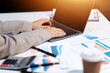 © Sutthicha - Business woman using calculator and writing make note with calculate. Woman working at office with laptop and documents on his desk