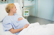 © wavebreak3 - Pregnant woman wearing hospital gown lying on bed resting hand on rounded abdomen beside IV pump