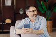 © deagreez - Confident mature man with beard using smartphone indoors enjoying stylish interior and relaxed moment