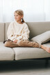 © SHOTPRIME STUDIO - Authentic lifestyle image of a young girl seated on a sofa in a cozy home setting, wearing casual clothes, calm and thoughtful, capturing everyday school life and play moments.