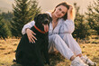 © KatyaPulka - Happy young woman smiling and hugging her black labrador dog outdoors in a natural setting with trees. Captures the bond between a pet owner and her companion.