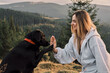 © KatyaPulka - A smiling woman high-fives her black Labrador Retriever in a mountain setting. Showcasing the special bond between humans and pets. Ideal for themes of companionship and outdoor adventures.