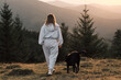 © KatyaPulka - Woman in sportswear walks her dog in the mountains at sunset.  Scenic view, outdoor recreation, and healthy lifestyle concept. A perfect image for active living.