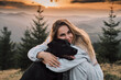 © KatyaPulka - A young woman embraces her black Labrador retriever at sunset in the mountains. The soft light and scenic backdrop create a heartwarming and peaceful scene, perfect for pet lovers.