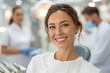 © kuchina - Portrait of a happy woman in a dentist chair smiling after successful teeth whitening procedure at dental clinic, with staff in the background.