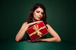 © Beauty Hero - Amazing brunette woman holding a red gift box with gold ribbon against green background, celebrating holiday