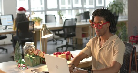 African American man wearing antlers preparing holiday report on laptop at office desk, copy space