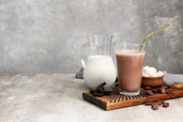 Wall Mural - Glass of sweet chocolate milk with cocoa beans and cubes of sugar on grey background