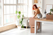 © Pixel-Shot - Young happy redhead businesswoman packing cardboard box of belongings with tape dispenser in office on moving day