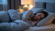 © creativemahfuz - Woman sleeping peacefully in bed at night, cozy bedroom setting with warm lamp light, comfortable sleepwear