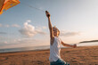 © Cavan Images - Boy reaching up flying a kite on beach at golden hour, copy space