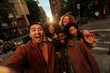 © bernardbodo - Happy multiracial friends taking photo of themselves while walking down the street