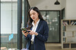 © Phimwilai - Businesswoman using smartphone in modern office, reading news and checking messages