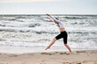 © TRAVELARIUM - Young woman performing graceful cartwheel on baltic sea shore. Overcast sky and rolling waves create dynamic backdrop. Energetic movement captured on sandy beach