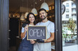© Dragana Gordic - Open Sign Moment: Happy Couple Owners Welcome Guests at Cozy Local Coffee Shop
