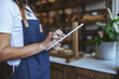 © Dragana Gordic - Baker in Denim Apron Using Tablet in Cozy Bakery Setting Demonstrating Modern Kitchen Management