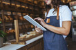 © Dragana Gordic - Smiling Woman In Denim Apron Using Tablet In Bakery Shop