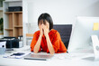 © laddawan - Asian woman overwhelmed at work, covering her face at a cluttered desk. Concept of stress, burnout, deadline pressure, and mental health in the workplace.
