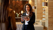 © PeopleVideos - Businesswoman helping customer or colleague in modern hotel lobby, using digital tablet for assistance or information