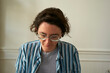 © Connect Images - Young woman with glasses and striped shirt looks down against a neutral background. Brussels, Belgium