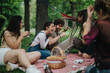 © qunica.com - A cheerful group of friends laughing and bonding during a picnic outdoors in a park. The warm and lively atmosphere emphasizes friendship and joy amidst a natural and relaxing environment.