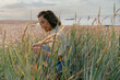 © Westend61 - Young woman sitting near timothy grass in front of sea at beach