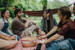 © qunica.com - Friends gather outdoors, sitting on a checkered blanket, enjoying food and conversation under trees.