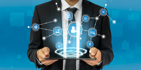 A businessman displays a tablet showcasing a holographic network of modern technology icons, illustrating digital communication and innovative business solutions. Tessel
