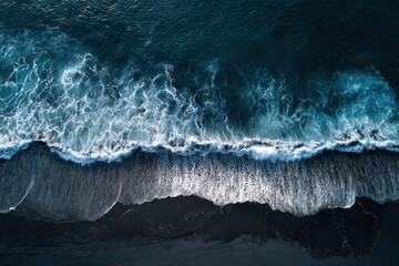 Wall Mural - Waves crashing on black sand beach captured from above during midday