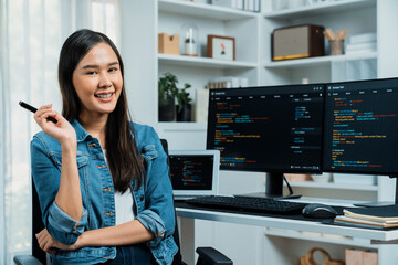Young Asian in IT developer looking at camera to present with online information on pc with coding program data application, wearing jeans shirt. surround by safety analysis two screens. Stratagem.