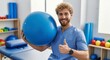 © phj.domingos - Physical therapist holding a large blue exercise ball and giving thumbs up