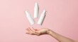 © PhotoHub - A hand gently tossing three white cosmetic pump bottles into the air against a soft pink background, suggesting a product launch or promotion