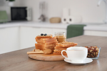 Wall Mural - Toasts with tasty peanut butter, nuts and cup of tea on table in kitchen, closeup