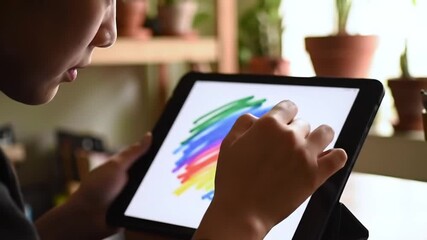 Close-up of a child's hands using a stylus to draw colorful strokes on a digital tablet screen