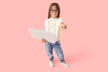 cute little schoolgirl with modern laptop pointing at viewer on pink background