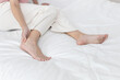 © Ratirat - women touching her painful heel while sitting on bed at home, representing heel pain, plantar fasciitis, Achilles tendon discomfort, or stress injury from standing or walking too long.